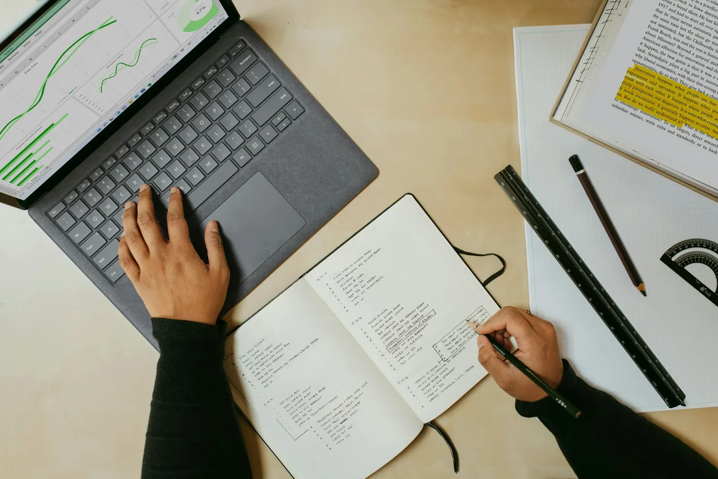 Una persona prende appunti su un quaderno accanto a un portatile con dei grafici